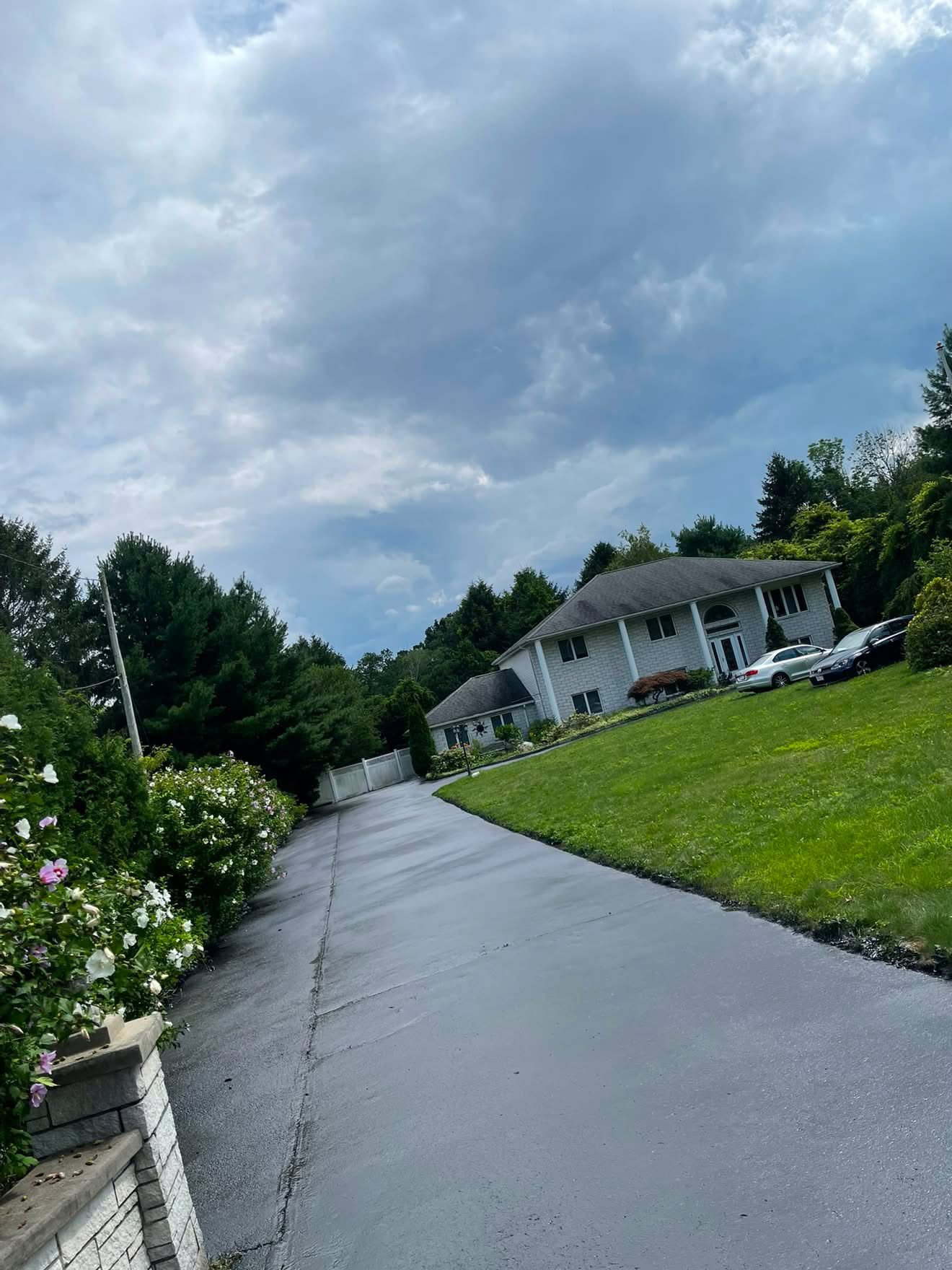 Sloped driveway sealed with a glossy black finish running up to a hillside home
